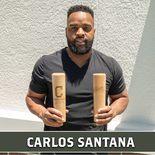 Carlos Santana holding two wooden Dugout Mugs baseball bat mugs with Cleveland team logos.