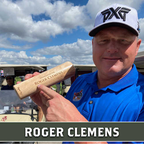 Roger Clemens holding a wooden Dugout Mugs baseball bat mug horizontally outdoors.