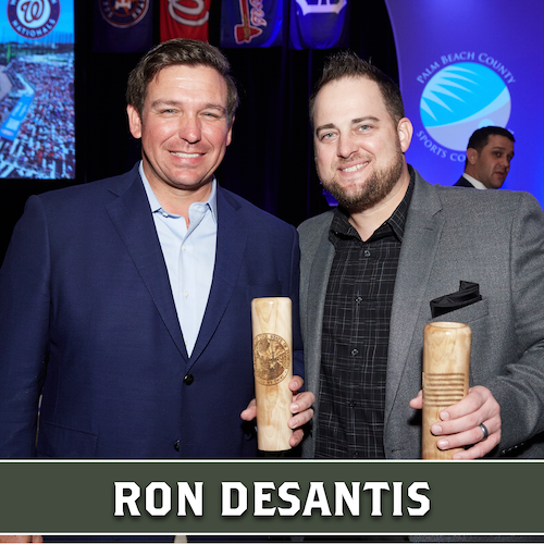 Ron DeSantis posing beside another man, both holding wooden Dugout Mugs baseball bat mugs.