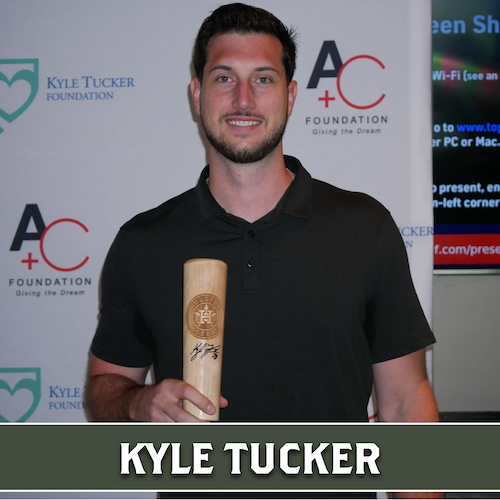 Kyle Tucker holding a wooden Dugout Mugs baseball bat mug in front of a foundation event backdrop.